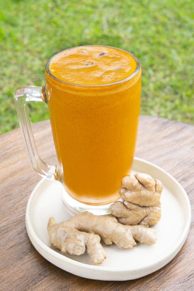 A tall glass of carrot and ginger juice with fresh ginger root on the saucer beside it