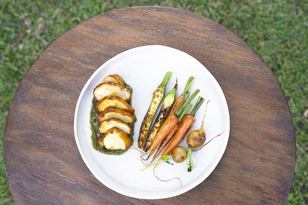 Roasted courgette, heirloom carrots and spring onions on a white plate with a green herb sauce