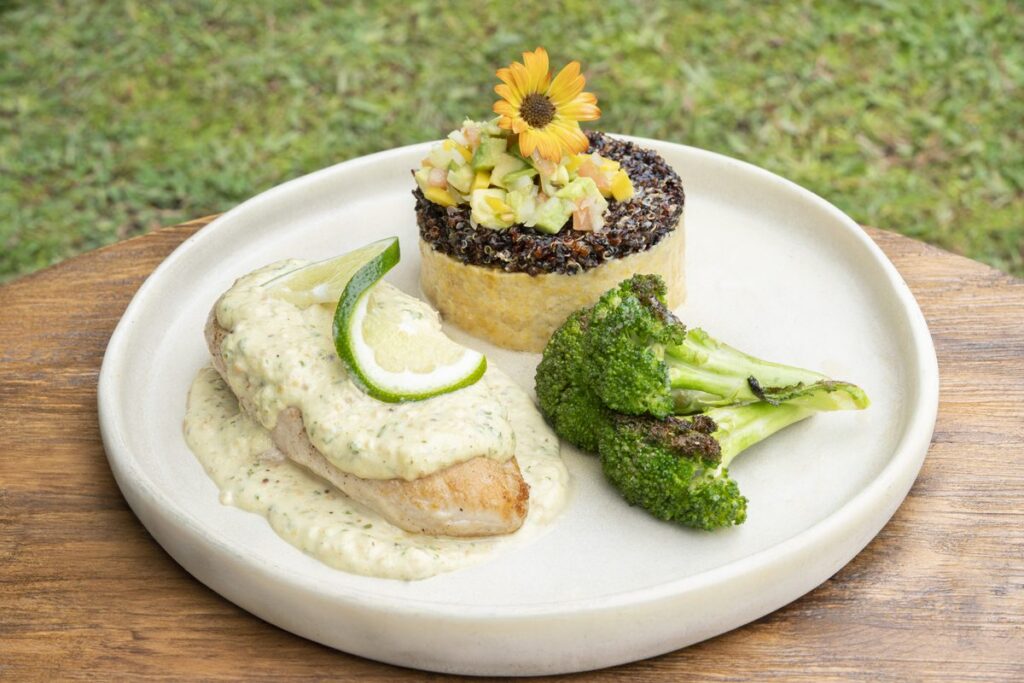 A plated main course — a fillet in a pale herb sauce with broccoli, lime and a grain timbale topped with an edible flower