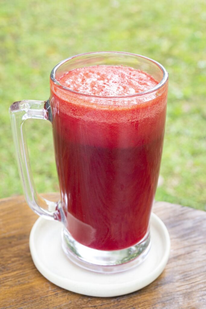 A tall glass of deep red beetroot juice on a wooden table