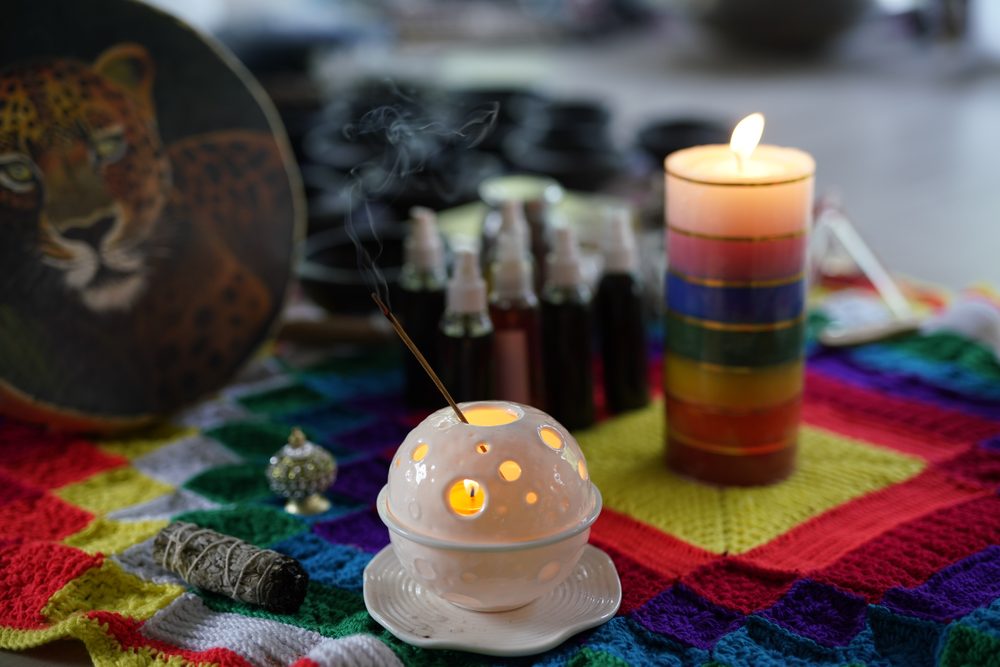 Ceremony objects laid on a woven blanket — a lit candle, incense, small bottles, dried herbs and a painted hide drum