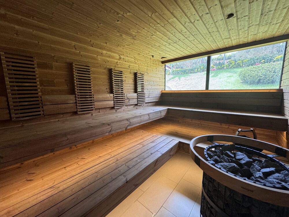 The timber-lined sauna with bench seating, a stone-filled heater and a window looking out over the grounds