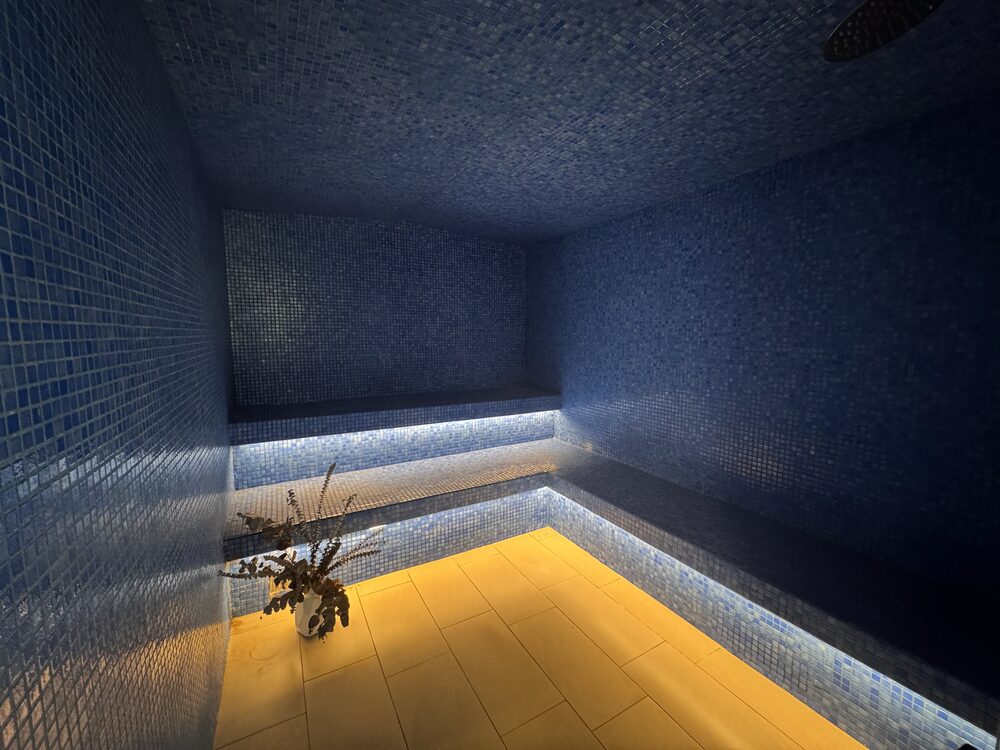 The steam room — a dark tiled chamber with a built-in bench and a low band of warm light along the floor