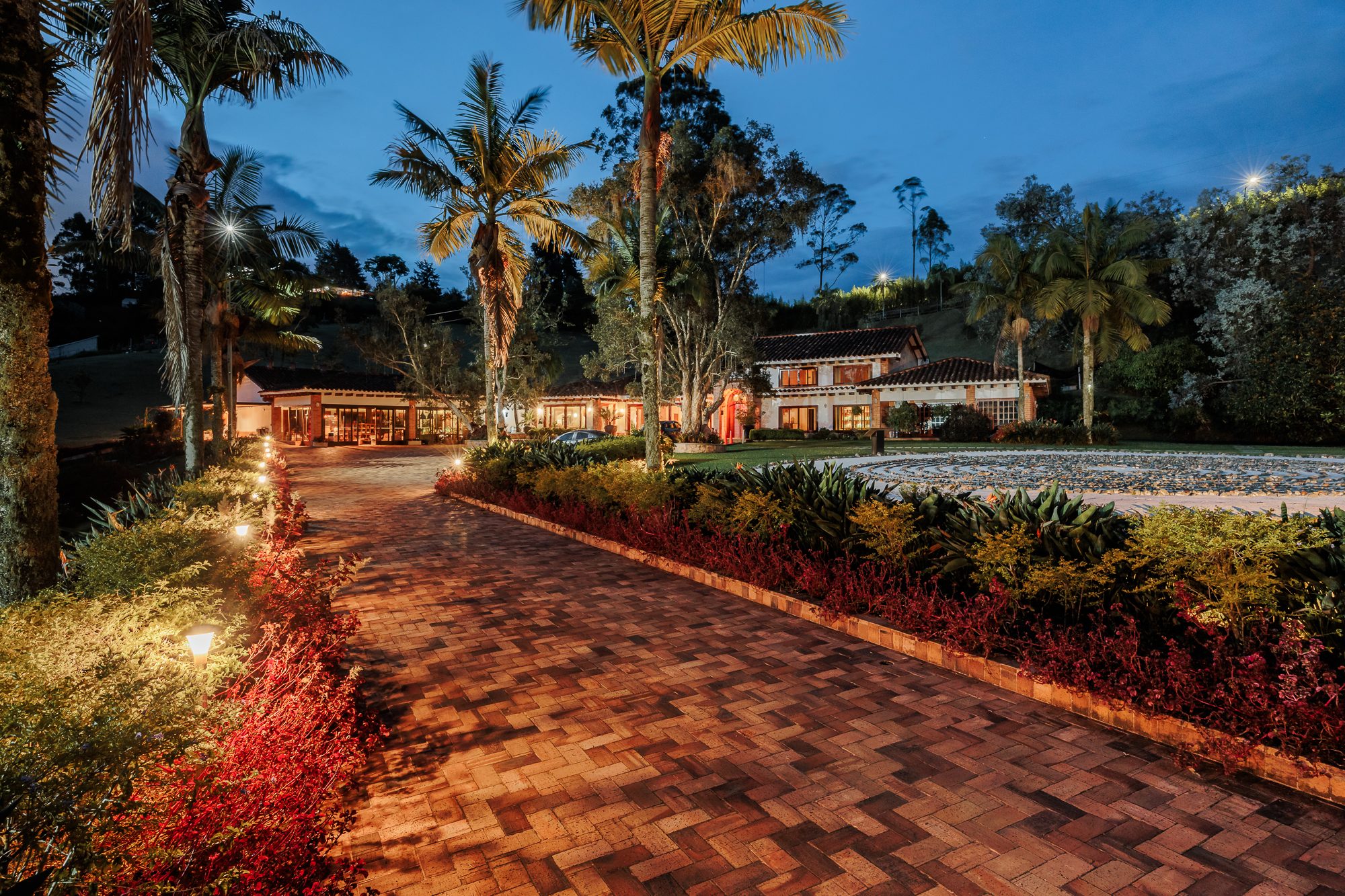 The brick driveway curving up to the main house at Mountains of Hope at dusk, framed by tall palms