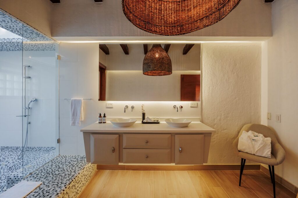 A guest bathroom with twin stone basins, a woven pendant lamp and a walk-in shower