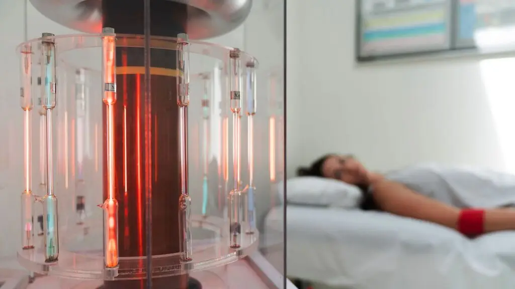 A BioCharger unit with its glass tubes lit, beside a person resting on a treatment couch