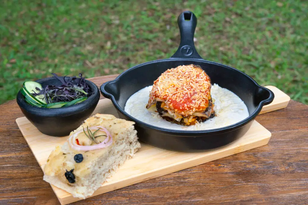 A skillet main with roasted vegetables and bread on a wooden board