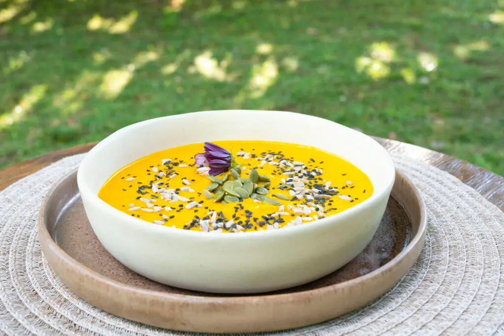 Golden soup topped with seeds in a white bowl