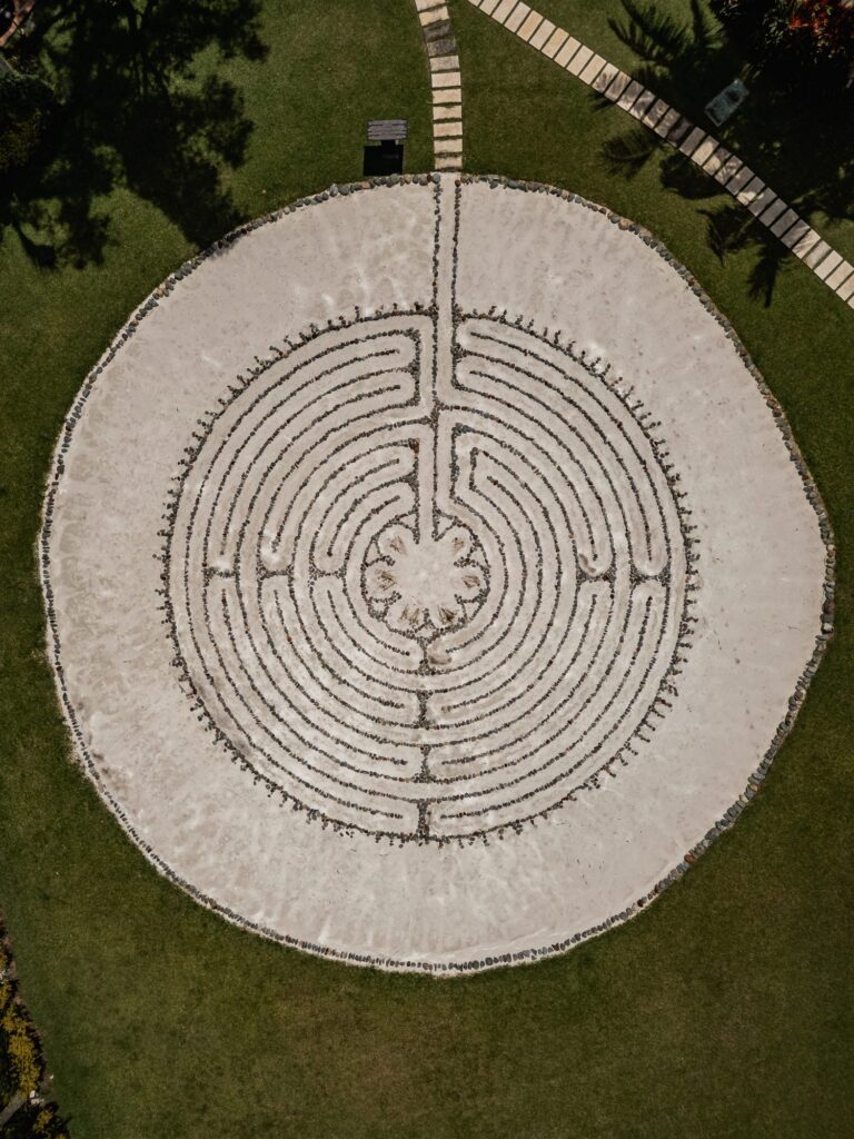 The circular stone labyrinth photographed from directly overhead, its pale walking path set into the grass