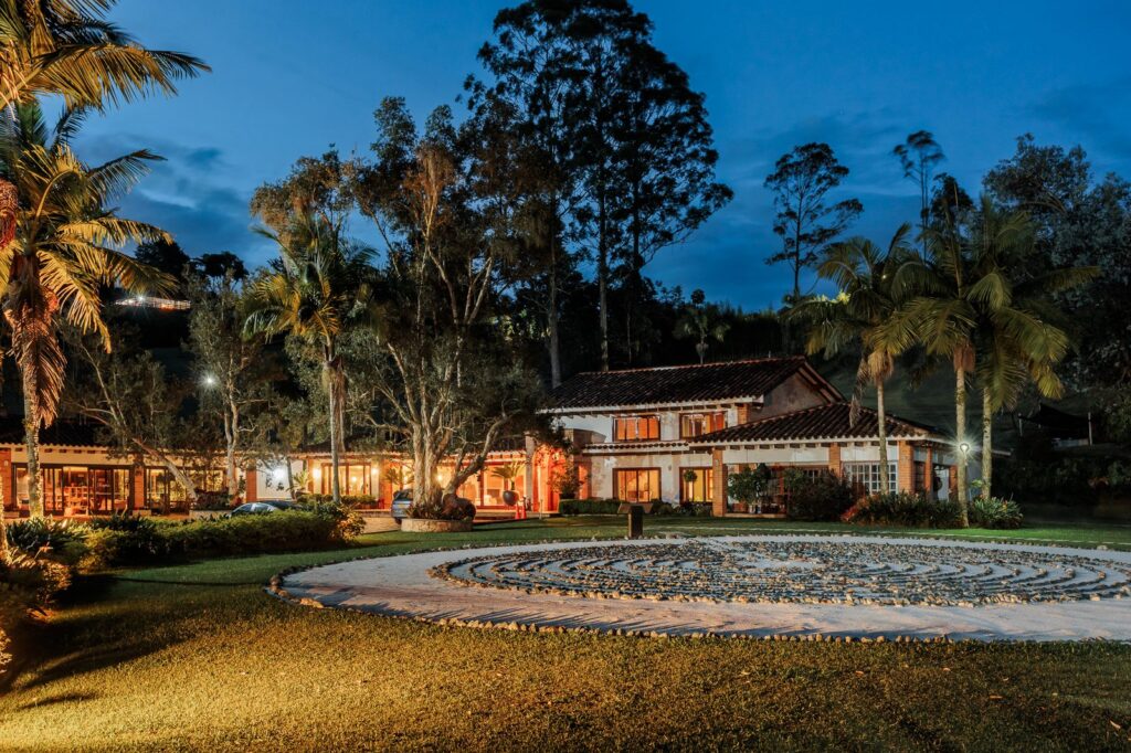 The labyrinth in the foreground at night, with the main house lit warm behind it under a deep blue sky