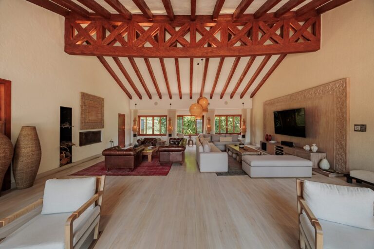 The main living room under carved timber beams, with long sofas, pale wood floors and tall windows