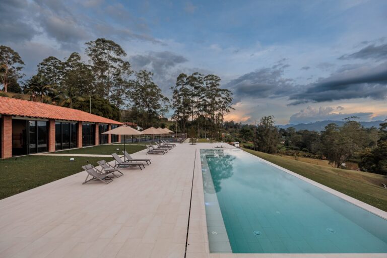 The lap pool and the long pavilion at dusk, with loungers along the deck and storm light over the trees