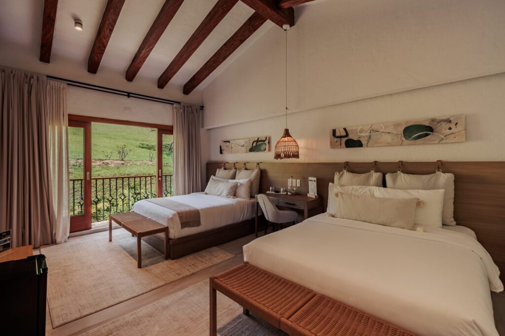 A twin guest room with two beds, a bench at the foot and glazed doors opening onto grass