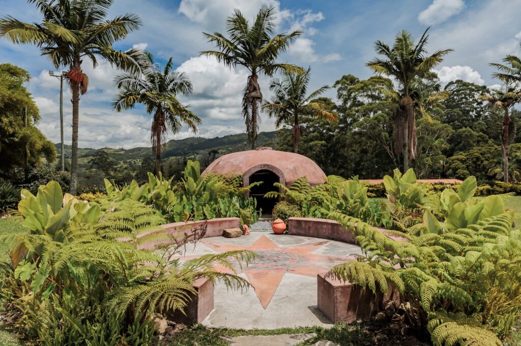 The domed temazcal set in planting at the treeline, with a tiled sun motif laid into the ground in front of it