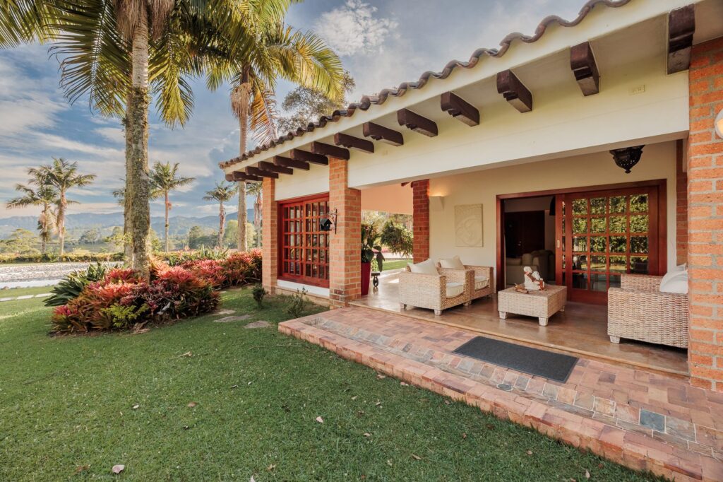 A covered terrace with wicker seating, opening straight onto the lawn with palms beyond