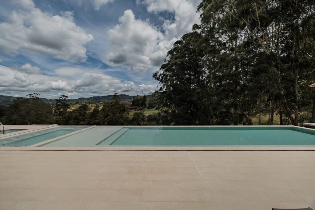 The lap pool and cold plunge under a wide cloudy sky, with the treeline and hills behind