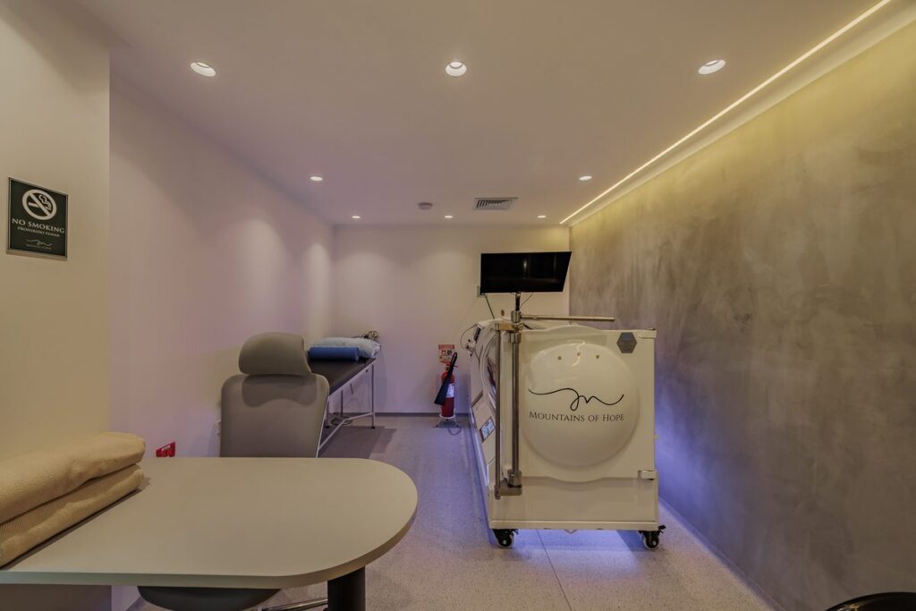 The treatment room housing the hyperbaric oxygen chamber, with a recliner and folded linens alongside